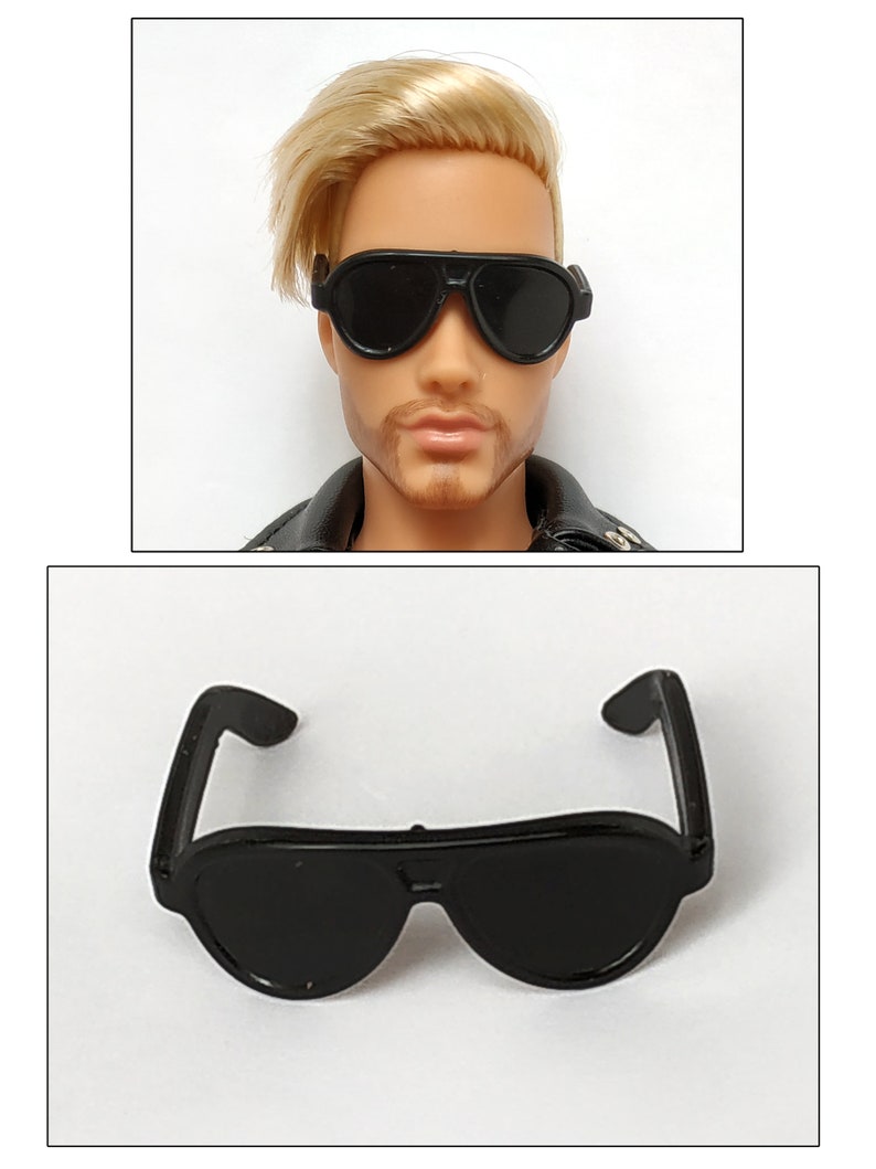 K&ouml;nnte beinhalten: Schwarze Plastik-Sonnenbrille mit abgerundeter Aviator-Form. Die Sonnenbrille ist f&uuml;r eine Puppe oder eine Actionfigur konzipiert.