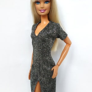 Puede incluir: Una mu&ntilde;eca rubia con un vestido plateado brillante con una abertura en el lateral.