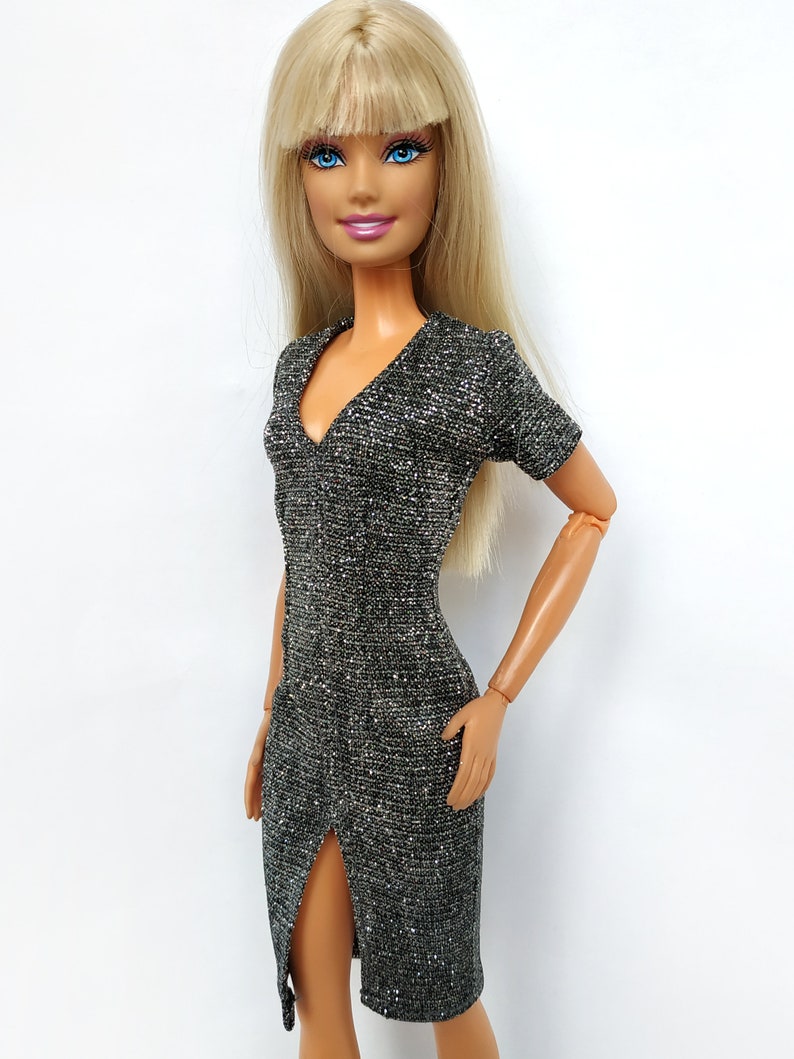 Puede incluir: Una mu&ntilde;eca rubia con un vestido plateado brillante con una abertura en el lateral.