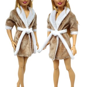 May include: Two blonde dolls wearing beige plush bathrobes with white trim and white sashes. The robes have long sleeves and a shawl collar.