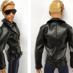 K&ouml;nnte beinhalten: Schwarze Lederjacke mit Rei&szlig;verschluss, G&uuml;rtel und goldenen Akzenten. Die Jacke hat einen Kragen und lange &Auml;rmel.