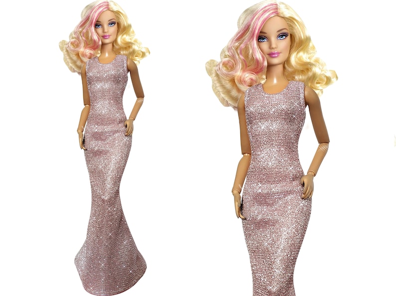 May include: A doll with blonde hair and pink highlights wearing a shimmering, rose-colored gown. The sleeveless dress has a fitted bodice and a flared, floor-length skirt. The doll has blue eyes and is posed against a white background.