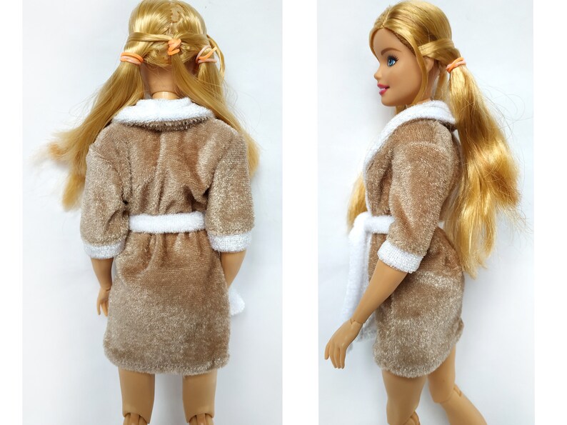 May include: A brown plush bathrobe with white trim and a white tie belt. The robe is worn by a doll with long blonde hair.