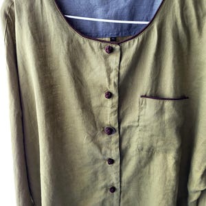 Puede incluir: Una camisa de lino verde con ribete marr&oacute;n y cierre de botones en la parte delantera. La camisa tiene un bolsillo en el lado izquierdo y una etiqueta que dice "Kuskoon Apparel" en el interior del cuello.