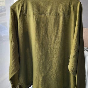 Puede incluir: Una camisa de lino verde oliva de manga larga con cuello en V y corte holgado.