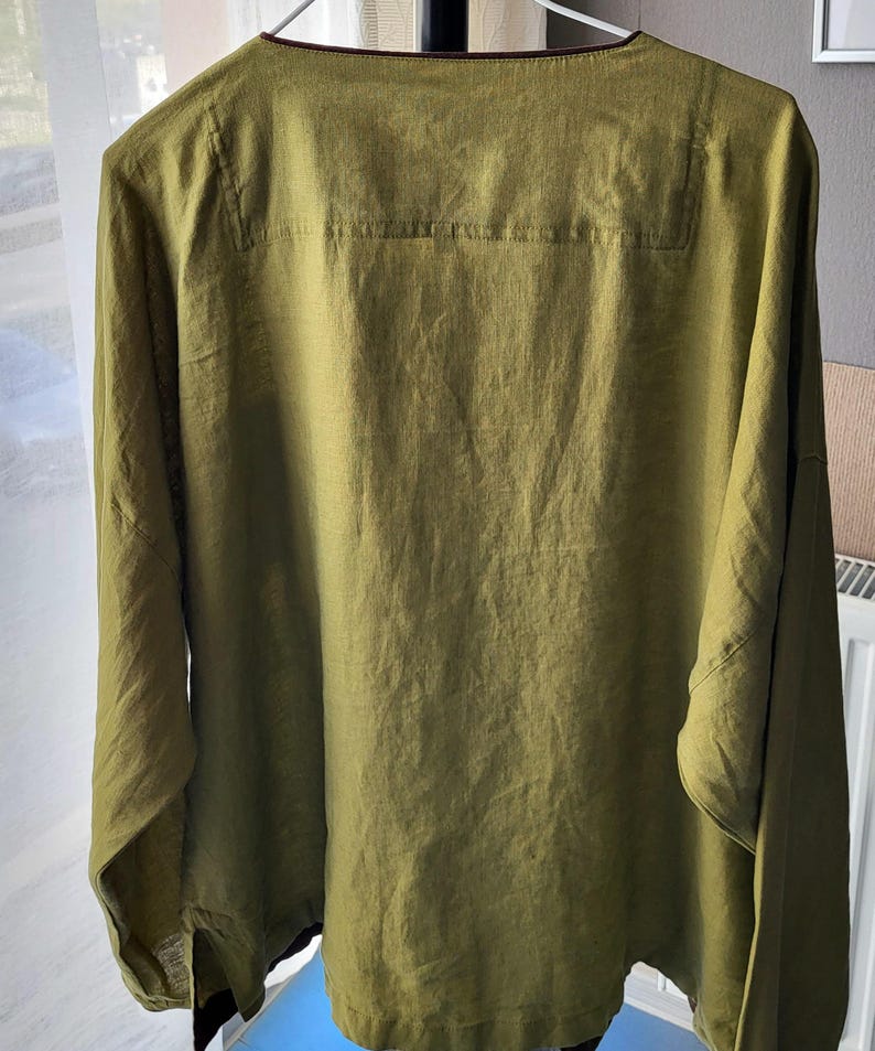 Puede incluir: Una camisa de lino verde oliva de manga larga con cuello en V y corte holgado.