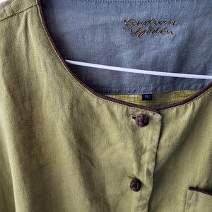 Puede incluir: Una camisa de lino verde con ribetes y botones marrones. La camisa tiene un cuello mandar&iacute;n y una etiqueta que dice "Runaway Sprinkles" y "XL".