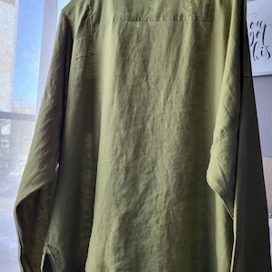 Puede incluir: Una camisa de lino verde con un escote redondo ancho y mangas largas. La camisa tiene un corte holgado y una silueta ligeramente oversized.