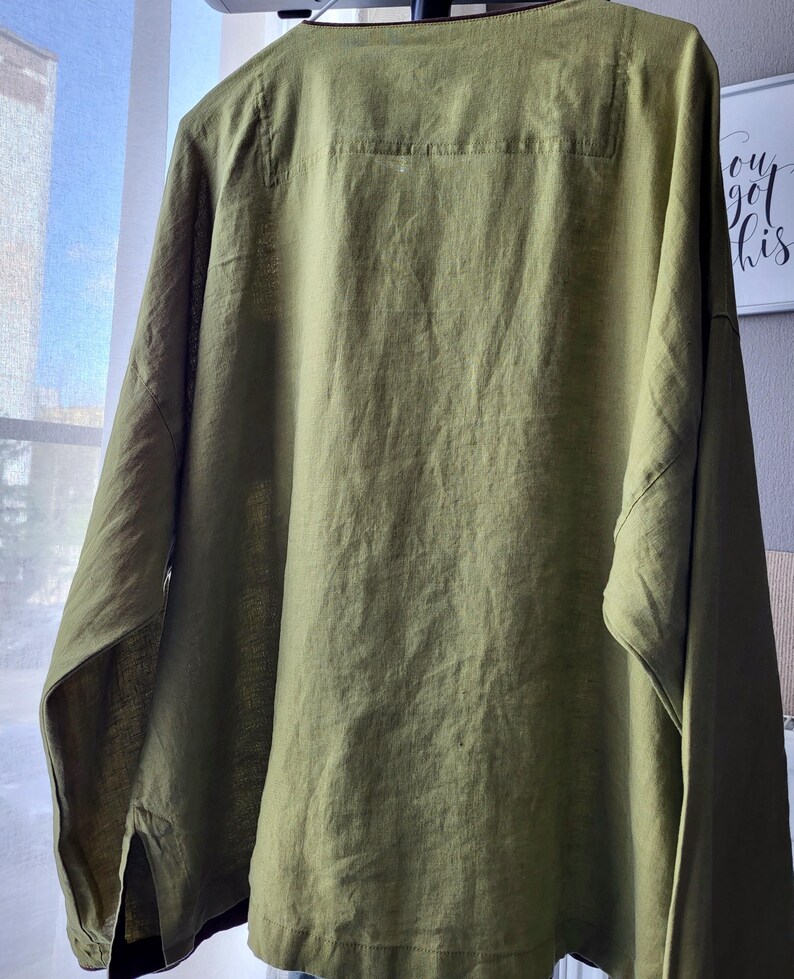 Puede incluir: Una camisa de lino verde con un escote redondo ancho y mangas largas. La camisa tiene un corte holgado y una silueta ligeramente oversized.