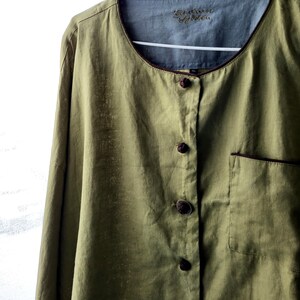 Puede incluir: Una camisa de lino verde con ribete marr&oacute;n alrededor del cuello y los bolsillos. La camisa tiene un frente abotonado con botones anudados. La etiqueta de la camisa dice "Embroidered Garden".