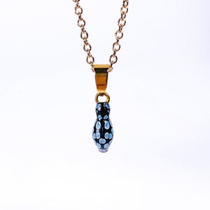 May include: A gold chain necklace with a black and blue pendant shaped like a frog. The pendant has a spotted pattern.
