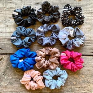 May include: Assortment of 10 colourful scrunchies in various patterns and colours, including blue, pink, gold, black, white, and grey. The scrunchies are made of fabric and have a gathered, ruffled look.