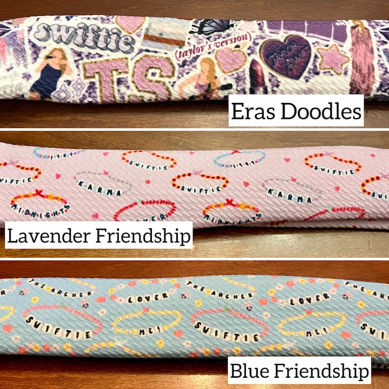 May include: Three fabric headbands with different patterns. The top headband is purple and white with a variety of images and text, including "Swiftie" and "Eras Doodles". The middle headband is lavender with a repeating pattern of hearts and the text "Swiftie" and "Karma". The bottom headband is blue with a repeating pattern of hearts and the text "Swiftie" and "Lover".