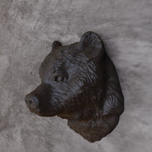 May include: A dark brown bear head sculpture mounted on a grey wall. The bear's head is facing to the left, and its eyes are closed.