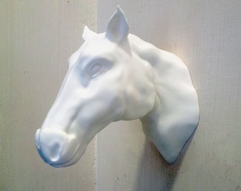 May include: White ceramic horse head sculpture mounted on a wall. The sculpture is a realistic depiction of a horse's head, with detailed features such as the eyes, nostrils, and mane.