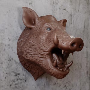 May include: A brown, wall-mounted sculpture of a boar's head with open mouth and visible tusks. The sculpture has detailed fur texture and is mounted on a textured gray wall. The boar's head is a decorative item.