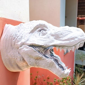 May include: A white plastic dinosaur head sculpture mounted on a wall. The dinosaur's mouth is open, revealing sharp teeth. The sculpture is a realistic depiction of a Tyrannosaurus Rex.