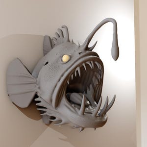 May include: A gray anglerfish wall sculpture with sharp teeth and a glowing lure. The fish has detailed fins and a textured surface, mounted on a neutral-colored wall. The sculpture is a unique piece of home decor.