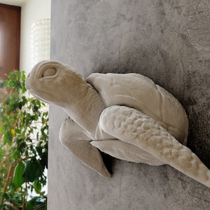 May include: A white ceramic sculpture of a sea turtle with its head turned to the side, mounted on a gray wall.