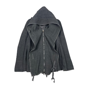 May include: A charcoal grey hooded jacket with a full-length zip and attached hood. The jacket features a distinctive design with a draped front and tie fastenings. The fabric appears to be a textured knit material. The label on the jacket is visible.