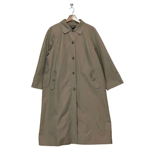 Puede incluir: Una gabardina larga de color beige con cierre de botones y dos bolsillos con solapa. La gabardina tiene un diseño clásico y es perfecta para superponer en climas más frescos.