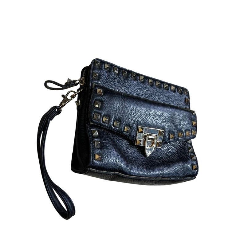 May include: Black leather crossbody bag with gold-tone pyramid studs. The bag features a flap closure with a silver-tone clasp and a wrist strap. The bag is rectangular in shape and has a textured surface.