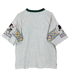 Puede incluir: Camiseta gris con cuello verde y mangas cortas. Las mangas presentan un colorido estampado geom&eacute;trico y una imagen de dibujos animados de Mickey Mouse. La palabra "MICKEY" es visible en las mangas.