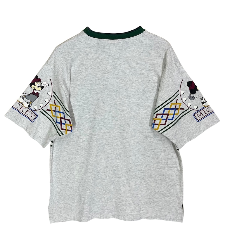 Puede incluir: Camiseta gris con cuello verde y mangas cortas. Las mangas presentan un colorido estampado geom&eacute;trico y una imagen de dibujos animados de Mickey Mouse. La palabra "MICKEY" es visible en las mangas.