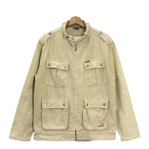 Könnte beinhalten: Hellbeige Jacke mit Reißverschluss, vier Vordertaschen und Knöpfen. Die Jacke hat einen Stehkragen und Schulterklappen. Die untere rechte Tasche hat ein kleines Logo. Die Jacke hängt an einem Holzkleiderbügel.