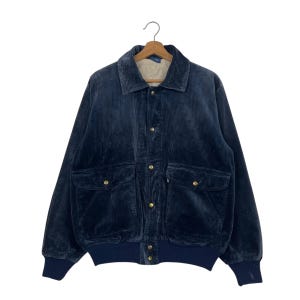 May include: A navy blue corduroy jacket with a button-up front, two front pockets, and a collared neckline. The jacket has a ribbed hem and cuffs. The jacket is hanging on a wooden hanger against a white background.