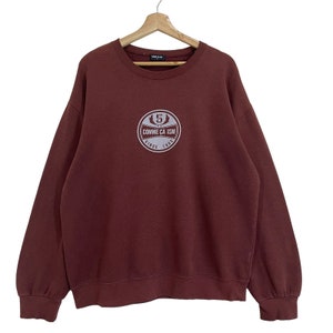 Puede incluir: Una sudadera color marrón con un logotipo blanco que dice "Comme Ca Ism" y "Since 1992".