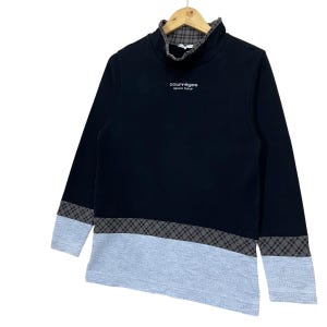 May include: Black long-sleeve sweatshirt with a high collar and gray and black plaid accents on the sleeves and lower hem. The sweatshirt has a gray lower panel and the text "courr&egrave;ges sport futur" in white.