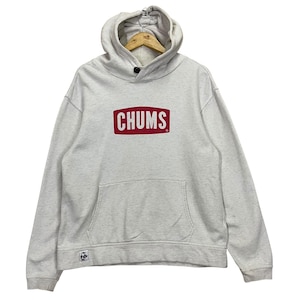 Puede incluir: Una sudadera con capucha gris claro con un bolsillo delantero y una capucha. La palabra "CHUMS" está impresa en un rectángulo rojo en el pecho. La sudadera tiene un cierre de botón en el cuello y un pequeño logotipo cerca del dobladillo inferior.