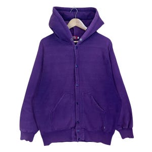 May include: A purple hooded sweatshirt with a button-up front closure and two front pockets. The sweatshirt is hanging on a wooden hanger. The fabric appears to be a soft, comfortable material.