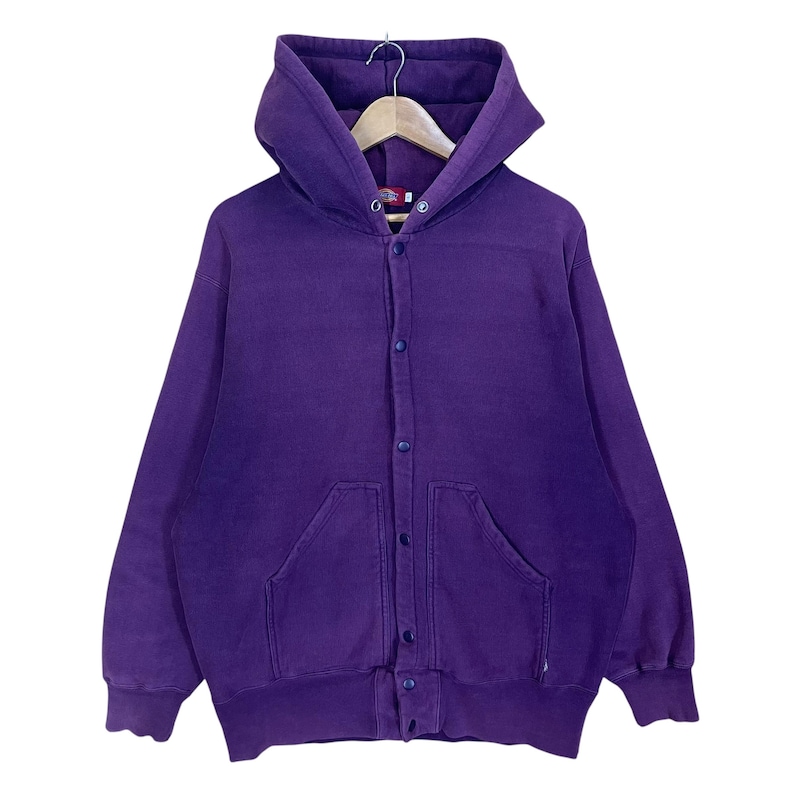 May include: A purple hooded sweatshirt with a button-up front closure and two front pockets. The sweatshirt is hanging on a wooden hanger. The fabric appears to be a soft, comfortable material.