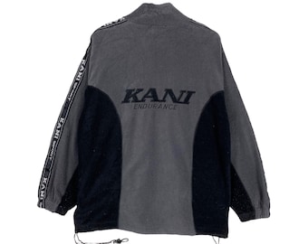 May include: A gray and black fleece jacket with a black KANI ENDURANCE logo on the back. The jacket has a zipper closure and a drawstring at the bottom.
