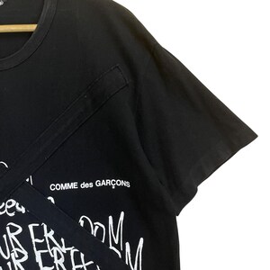 May include: Black t-shirt with a white graphic print that says "Comme des Gar&ccedil;ons" and has a white graphic print of a design with the words "freedom" and "room" repeated.