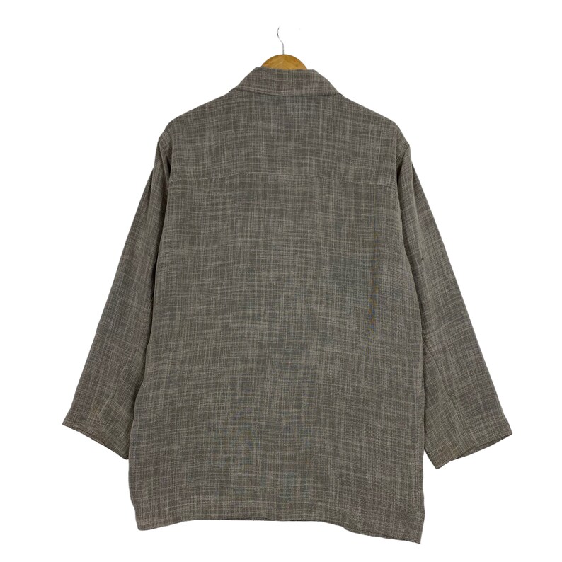 May include: A brown long-sleeved shirt with a textured pattern. The shirt is hanging on a wooden hanger.