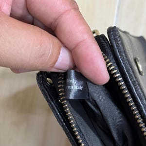 May include: Black leather wallet with a gold zipper and the text "Italy en Italy" on a small tag. The wallet is open, revealing a dark interior.