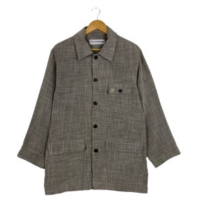May include: A brown and gray checkered long-sleeved shirt with a button-up front and two large pockets. The shirt has a small label on the front that says "Universal Works".