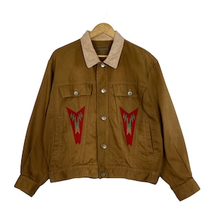 Könnte beinhalten: Eine braune Jeansjacke mit einem Cordkragen und einem geometrischen Muster auf dem Rücken. Das Muster ist in Rot, Grün und Weiß.