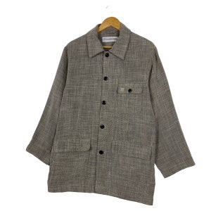 May include: A brown long-sleeved button-up shirt with a textured woven fabric. The shirt has a collared neckline, two chest pockets, and black buttons.