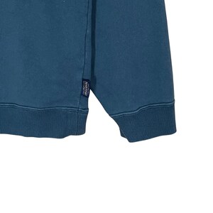 以下が含まれることがあります： ティール色のスウェットシャツのクローズアップ。スウェットシャツはクルーネックで、「Pendleton」という文字が入った小さな長方形のタグが付いています。生地は柔らかく快適な素材のようです。