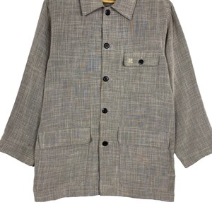 May include: A brown and gray long-sleeved button-up shirt with a small pocket on the left chest. The pocket has a white logo that says "HE".