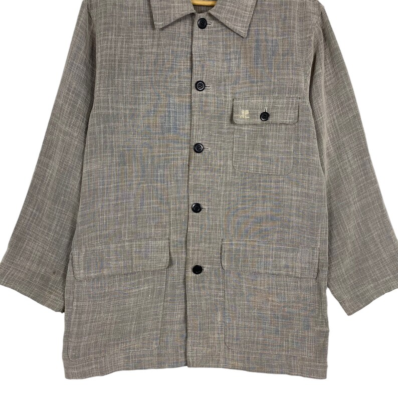 May include: A brown and gray long-sleeved button-up shirt with a small pocket on the left chest. The pocket has a white logo that says "HE".