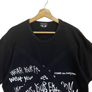 May include: Black t-shirt with white graffiti-style text that reads "Wear your f...weat your..." and "Comme des Gar&ccedil;ons".