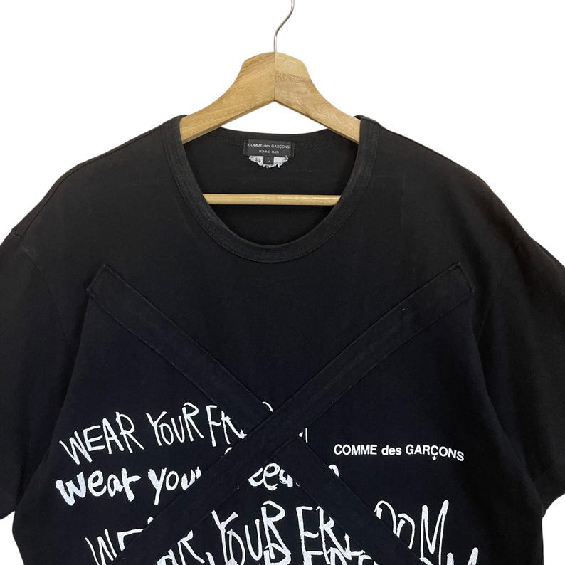 May include: Black t-shirt with white graffiti-style text that reads "Wear your f...weat your..." and "Comme des Gar&ccedil;ons".
