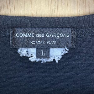 May include: Black t-shirt with a Comme des Gar&ccedil;ons Homme Plus label. The label is black with white text and a size tag that says "L".