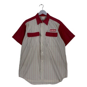 Puede incluir: Una camisa de trabajo de manga corta a rayas blancas y rojas con un parche rojo en el pecho derecho que dice "ENEOS".