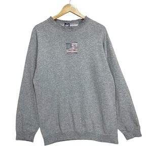 May include: A gray crew neck sweatshirt with a small embroidered American flag design on the chest. The flag is red, white, and blue. The text "DC SHOES USA" is below the flag. The sweatshirt is hanging on a wooden hanger.